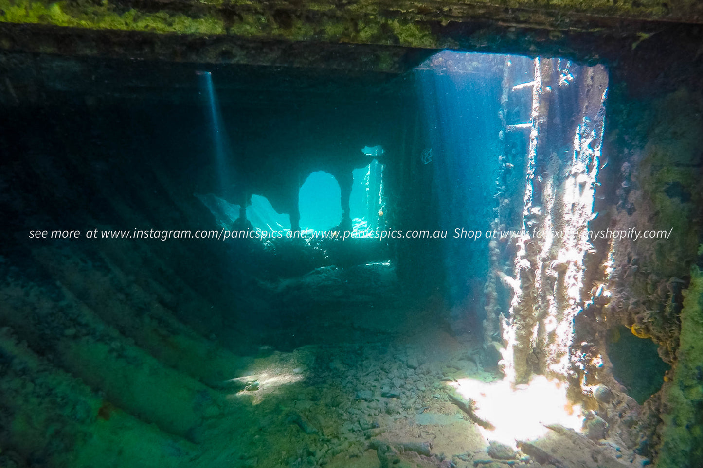 Underwater view of a sunken ship with sunlight filtering through the water.