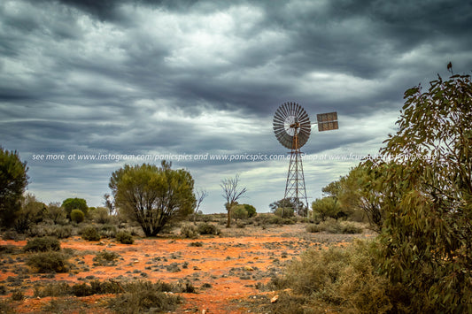 Desert landscape with a windmill under a stormy sky