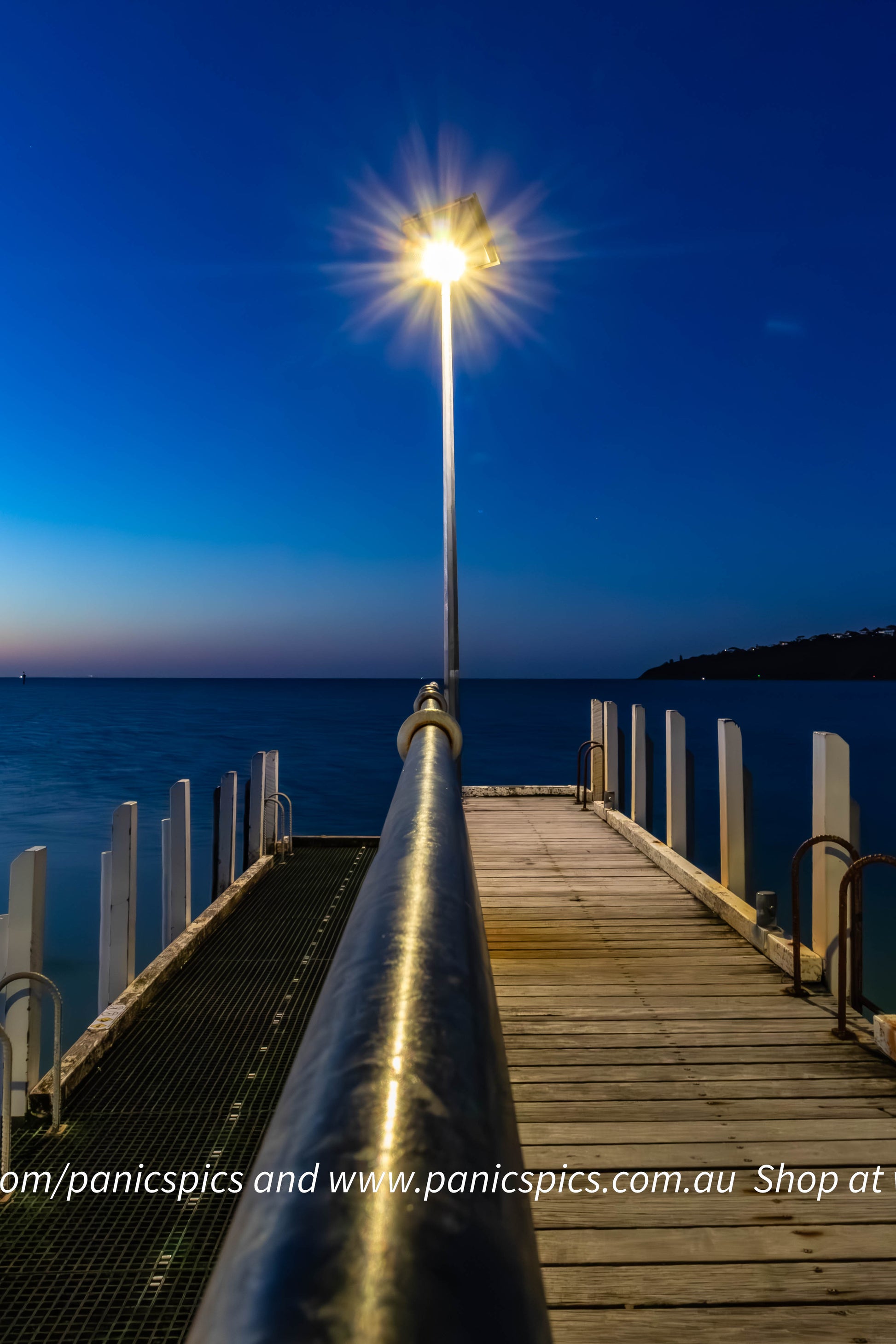 Wooden pier extending into the water with a light pole at night.
