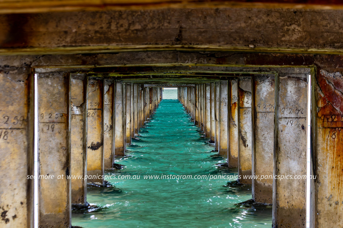 View through a pier with concrete pillars and turquoise water.