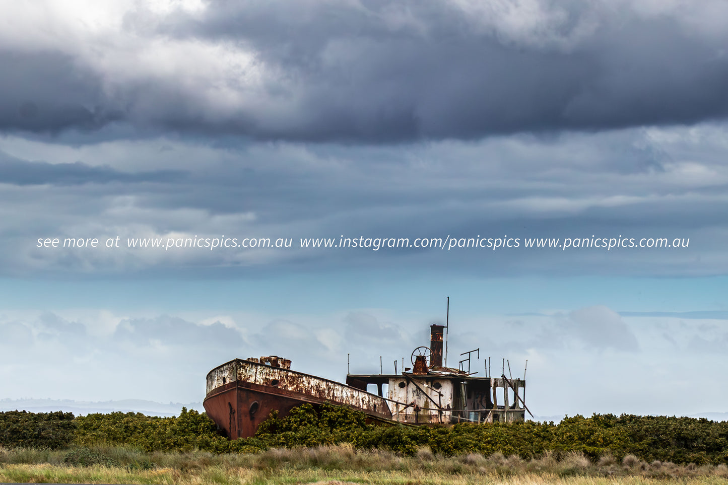 Rust-covered shipwreck on a grassy field with a dramatic sky.