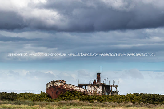 Rust-covered shipwreck on a grassy field with a dramatic sky.