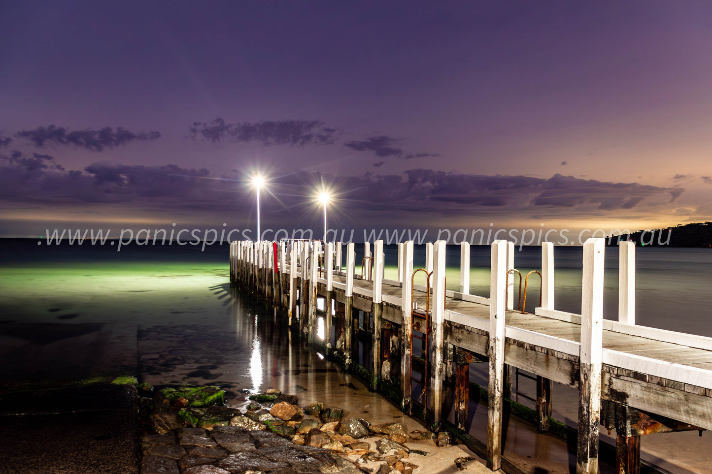 Wooden pier extending into the water at dusk with lights illuminating the scene.