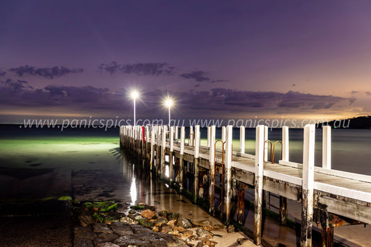 Wooden pier extending into the water at dusk with lights illuminating the scene.