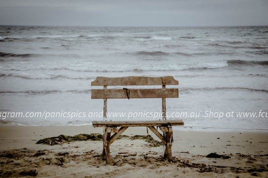 Wooden bench on a sandy beach with ocean waves in the background